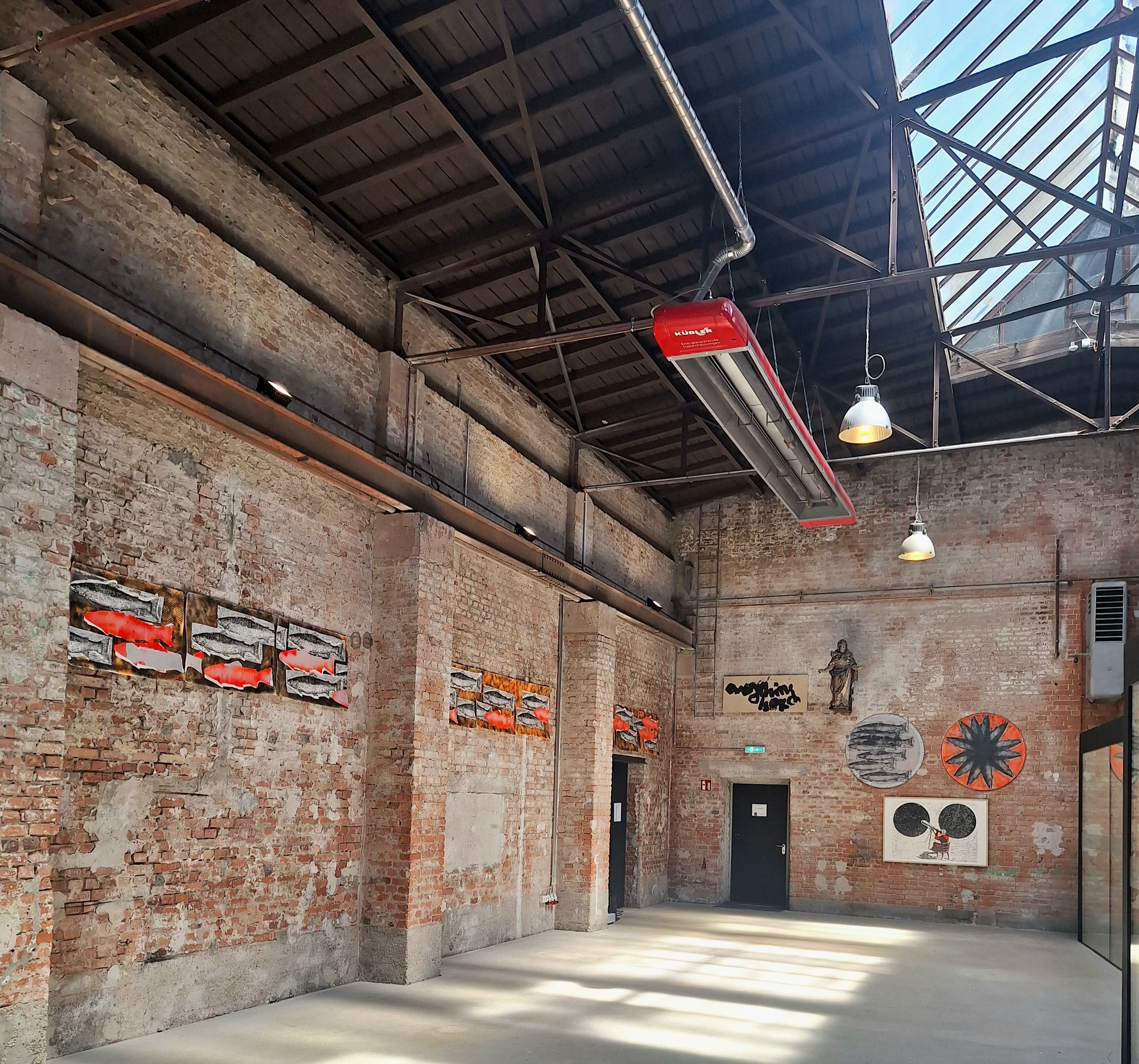 Hoher Ausstellungsraum mit Backsteinwänden, Glasdach und mehreren rot-weißen Arbeiten.