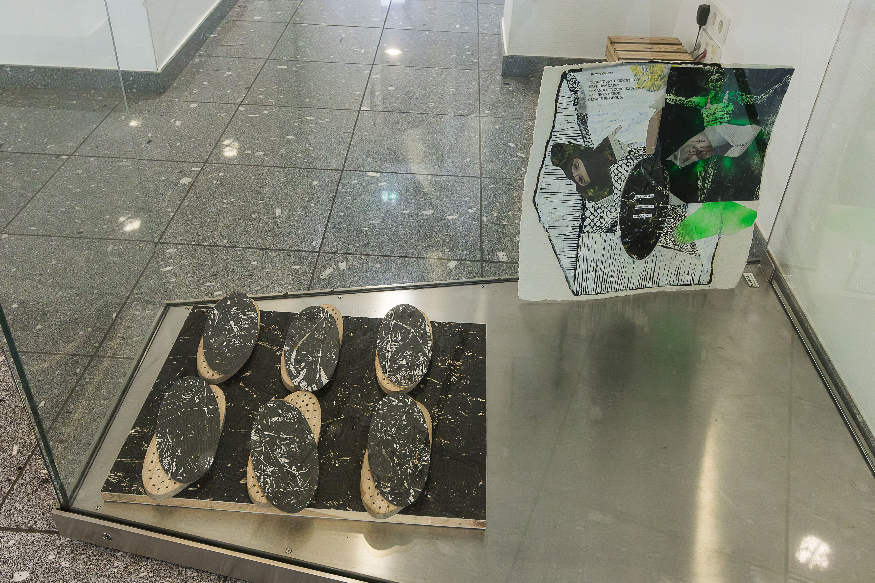 Blick in eine Glasvitrine mit dunklen runden Formen und einer grün-schwarzen Arbeit.