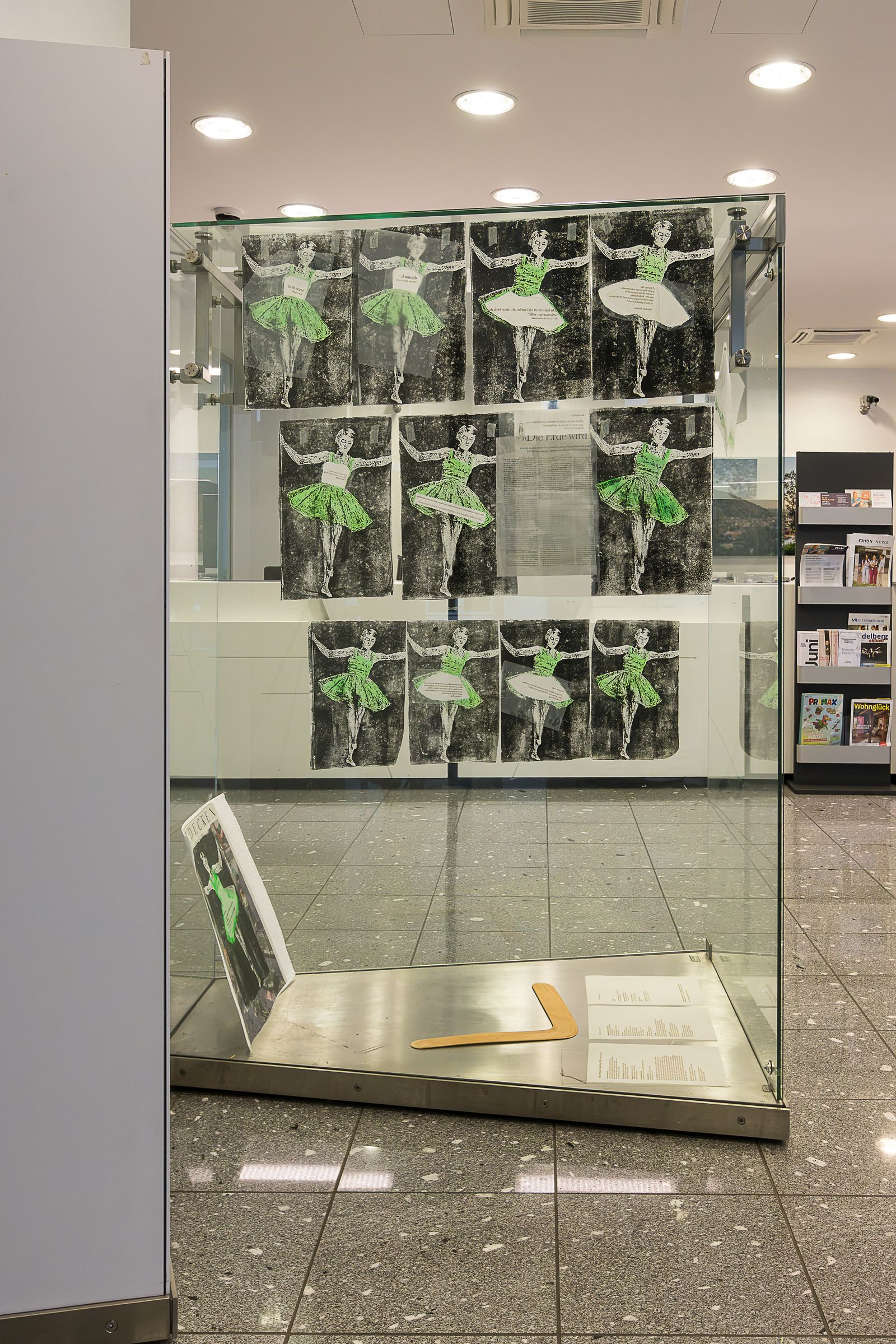 Ausstellungsansicht mit grün-schwarzen Arbeiten an einer Stellwand und einer Vitrine davor.