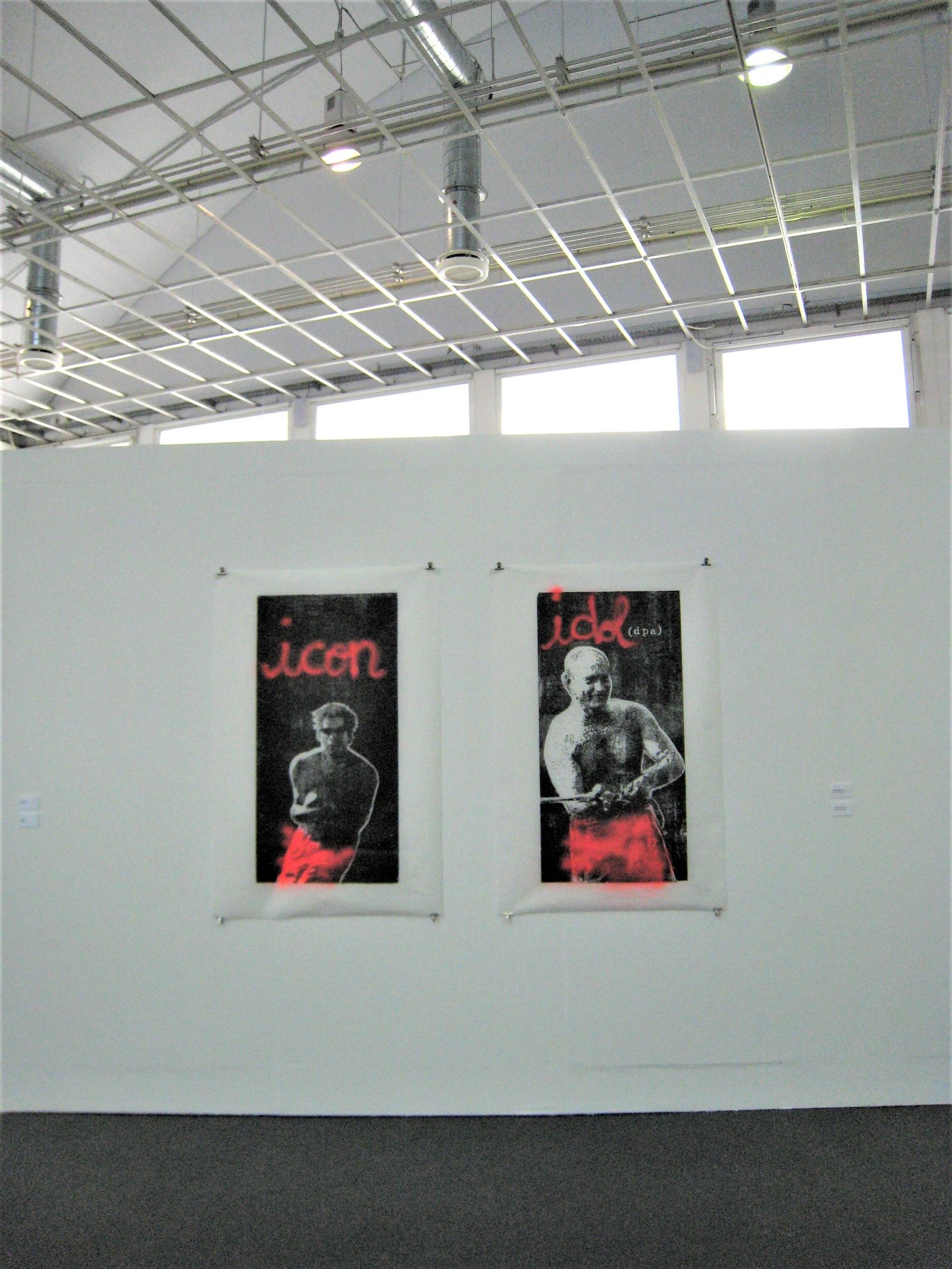 Zwei schwarz-rote Plakatarbeiten hängen an einer Wand in einem hellen Ausstellungssaal.
