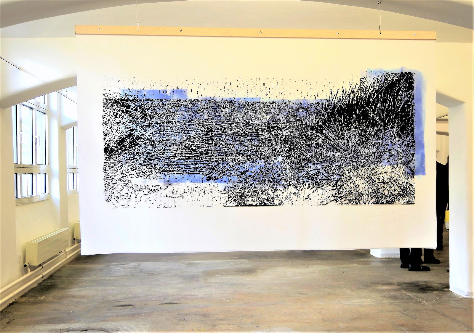 Großformatige schwarzweiße Arbeit erstreckt sich über eine Wand im hellen Ausstellungsraum.