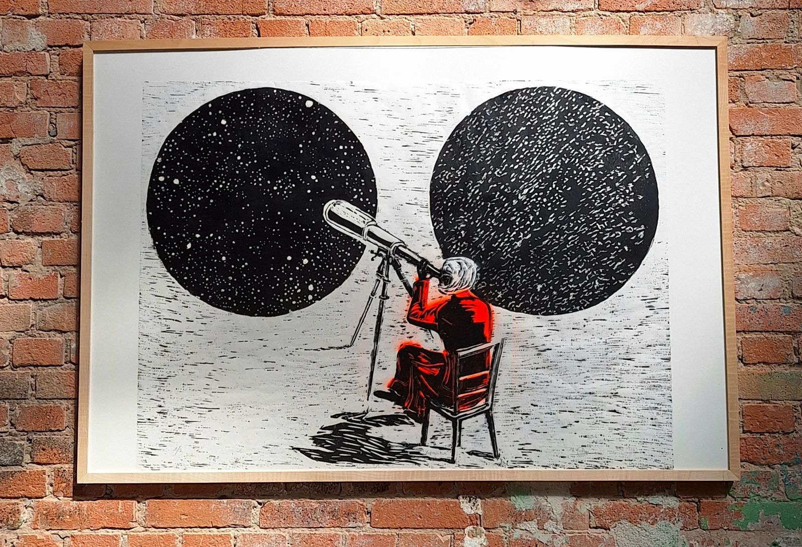 Gerahmte Arbeit an einer Backsteinwand: Eine rot gekleidete Figur blickt durch ein Fernrohr vor zwei dunklen Kreisen.