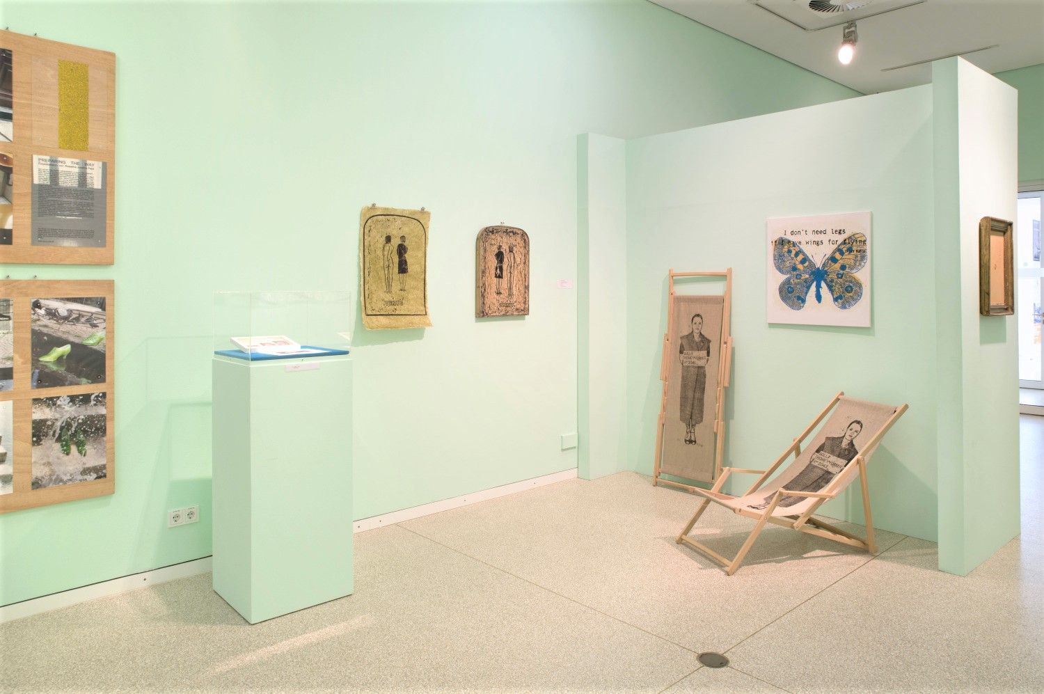 Ausstellungsraum mit mintgrünen Wänden, mehreren gerahmten Arbeiten und einem Stuhl.