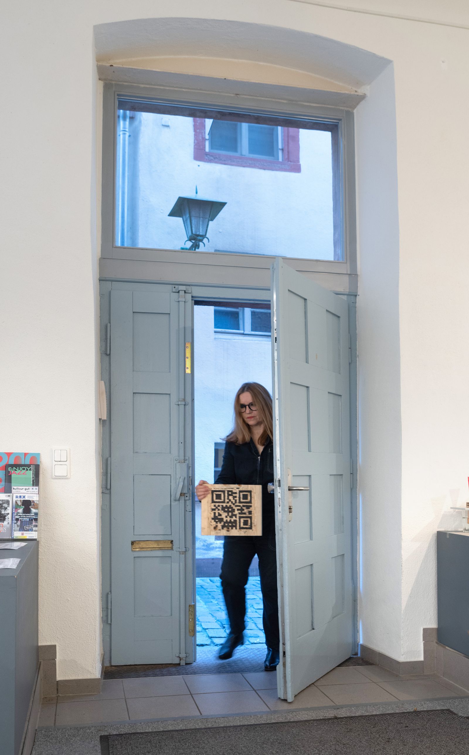 Person steht in der geöffneten Tür eines Ausstellungsraums und hält ein Bild.
